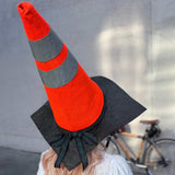 A blonde woman from behind, sporting an unconventional bike helmet fashioned from a bright orange traffic cone, merges safety with a touch of whimsy on her outdoor adventure.
