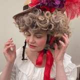 Woman adjusting the Hair Helmet 1789, a bicycle helmet styled with a curly powdered wig and feathered straw hat, blending 18th-century fashion with modern safety