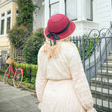 A woman wearing a red straw hat bike helmet gracefully walks down a sidewalk in a white dress