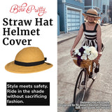 Woman riding a bike in a black and white dress wearing a straw hat bike helmet cover with flowers in the front basket; fashionable helmet accessory for stylish cyclists.