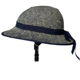 White background product photo. A helmet cover resembles a wide brim straw hat. It's shown installed on a bicycle helmet although only the chin strap of the helmet is visible. The plaiting of the helmet is a mix of off-white and navy blue twists creating a textured effect reminiscent of denim. The product is shown in a profile view.