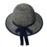 White background product photo. A helmet cover resembles a wide brim straw hat. It's shown installed on a bicycle helmet although only the chin strap of the helmet is visible. The plaiting of the helmet is a mix of off-white and navy blue twists creating a textured effect reminiscent of denim. The product is shown from the back. A navy blue hatband and bow are clearly visible.